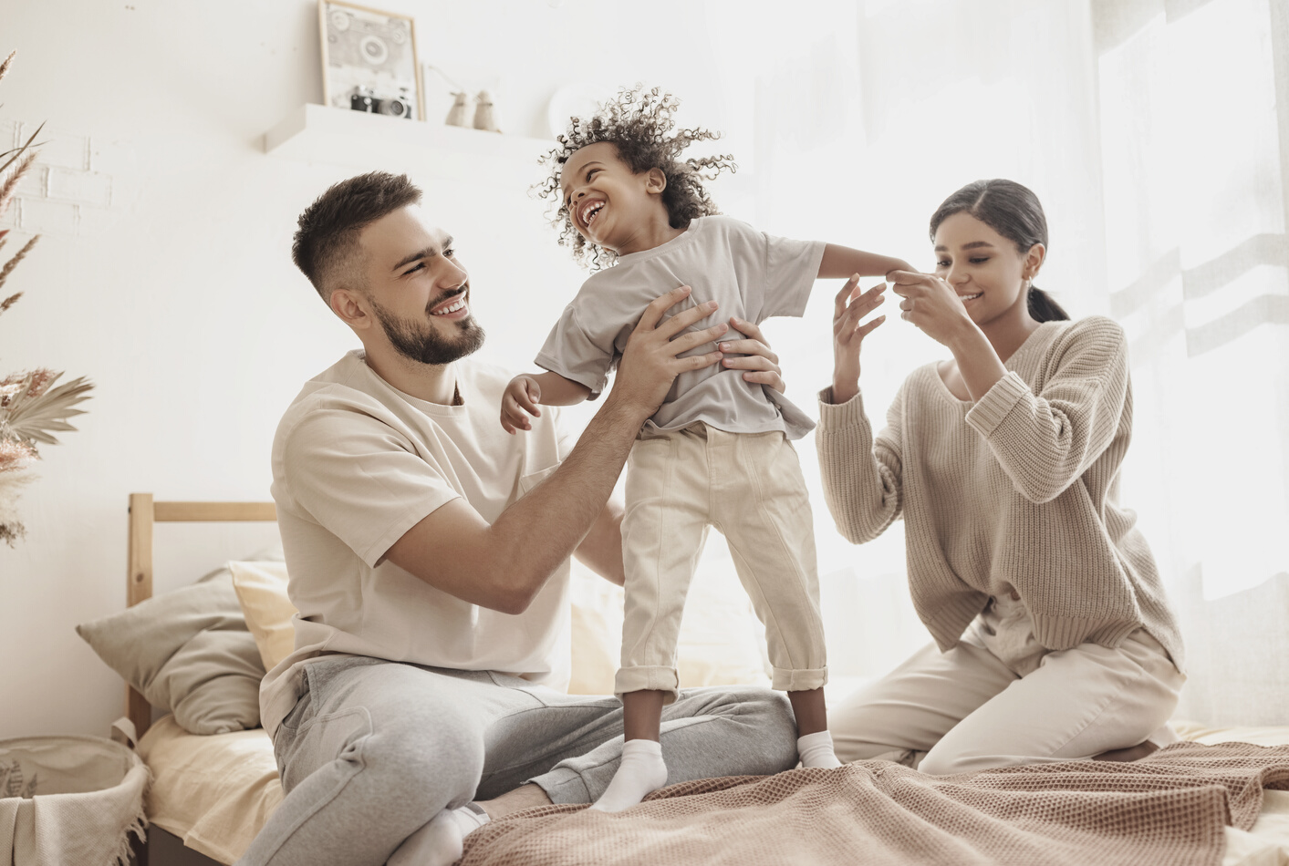 happy diverse family mom, dad and child  laughing, playing and jumping   in bed   at home